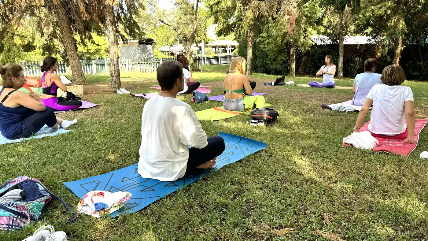 Μάθημα yoga κάτω από τα δέντρα του Πάρκου Φλοίσβου, με θέα τη θάλασσα.