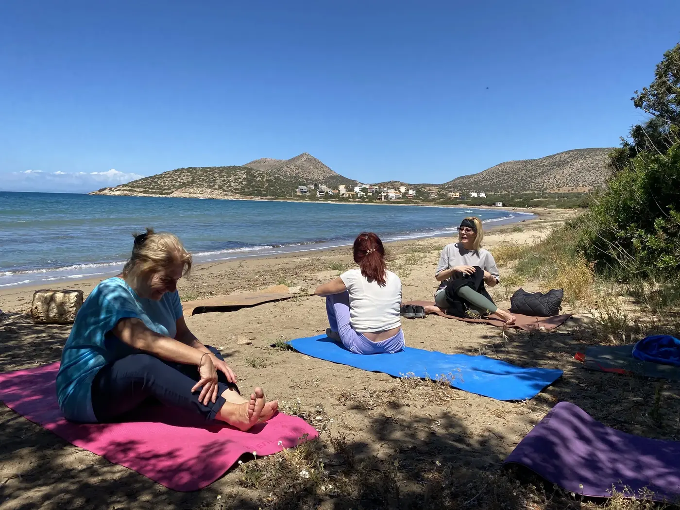 Ομάδα καθισμένη σε στρώματα γιόγκα δίπλα στη θάλασσα.